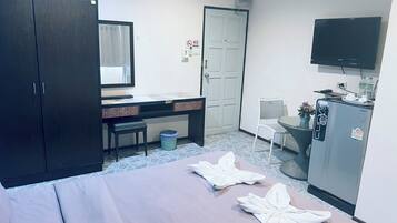 A hotel room with a bed, a desk, a chair, a television, and a minibar.