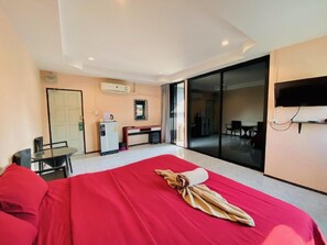 A hotel room with a bed, a desk, a chair, a television, and a sliding glass door leading to a balcony. - Apartment X5 (Pattaya)