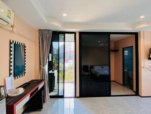 Quarto de hotel com porta de vidro deslizante que dá para uma varanda, uma cama, uma mesa de trabalho com cadeira e uma televisão fixada na parede.
