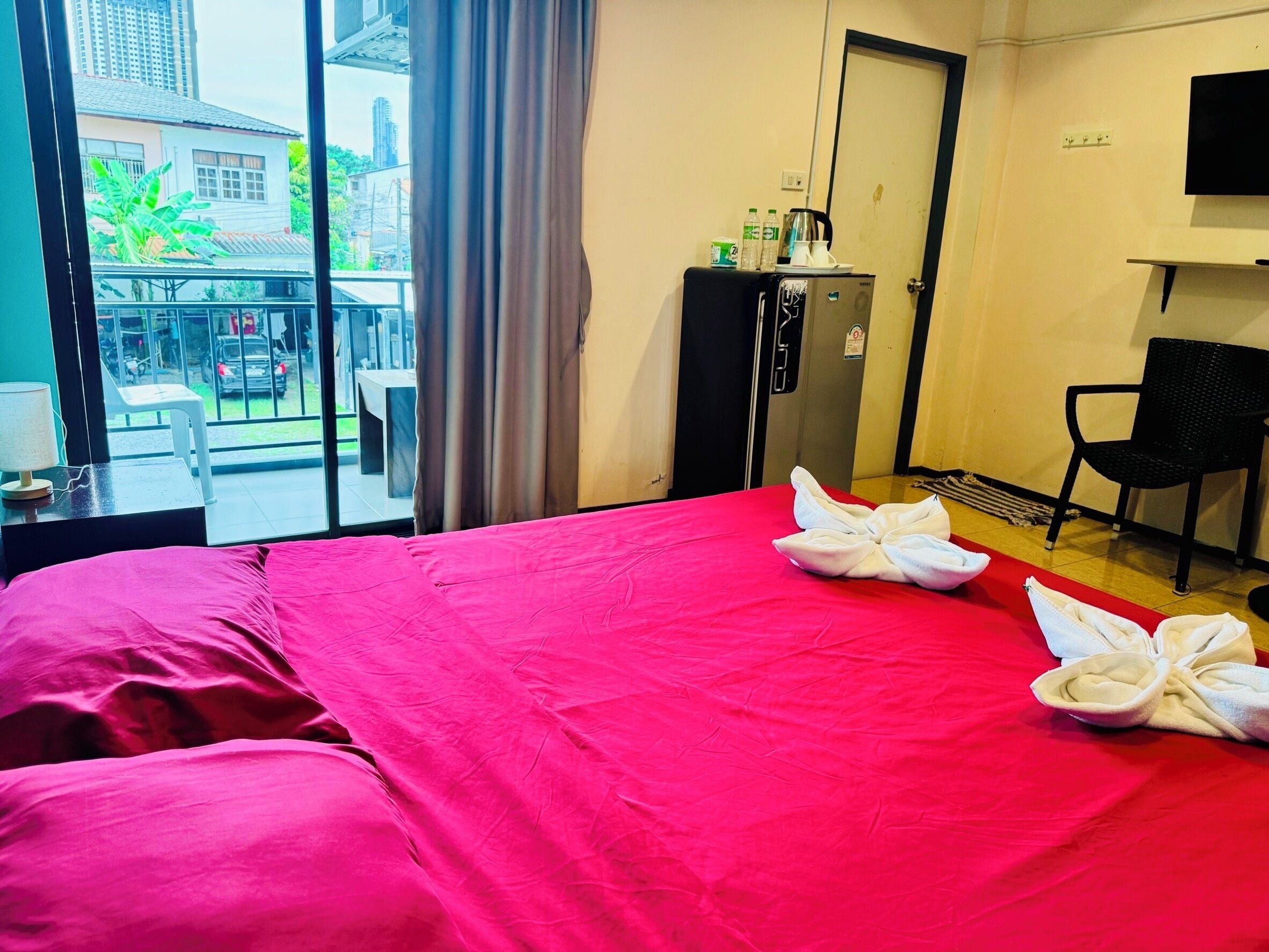 A hotel room with a bed, a desk, a chair, a minibar, and a view of the outside.