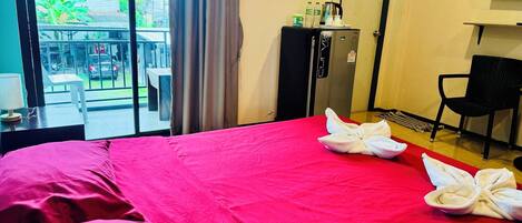 A hotel room with a bed, a desk, a chair, a minibar, and a view of the outside.