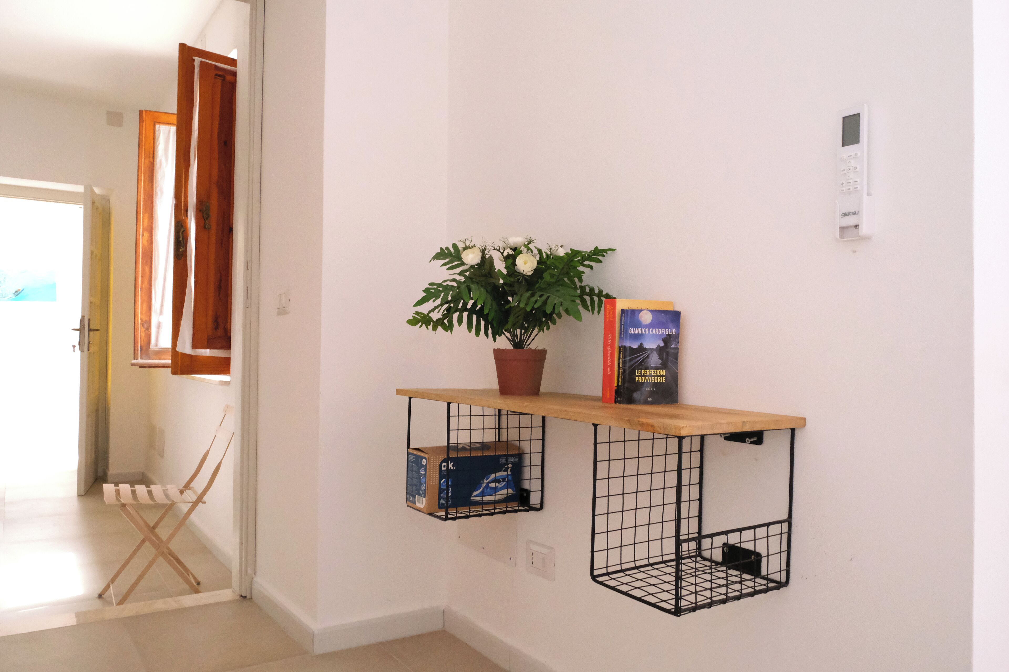 A hallway with a wooden door, a potted plant, a book, and a shoe box on a wire shelf.