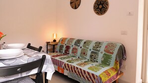 A dining area with a table set for four, a sofa with a colorful quilt, and two wall decorations. - Newly refurbished Apartment great location (Buggerru)