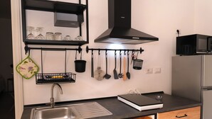 A kitchen with a stainless steel sink, a black microwave, and a range hood above the stove. - Newly refurbished Apartment great location (Buggerru)