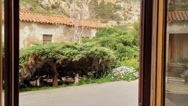 A view through a window of a building with a tiled roof, a stone wall, and a road leading to a hillside. - Newly refurbished Apartment great location (Buggerru)