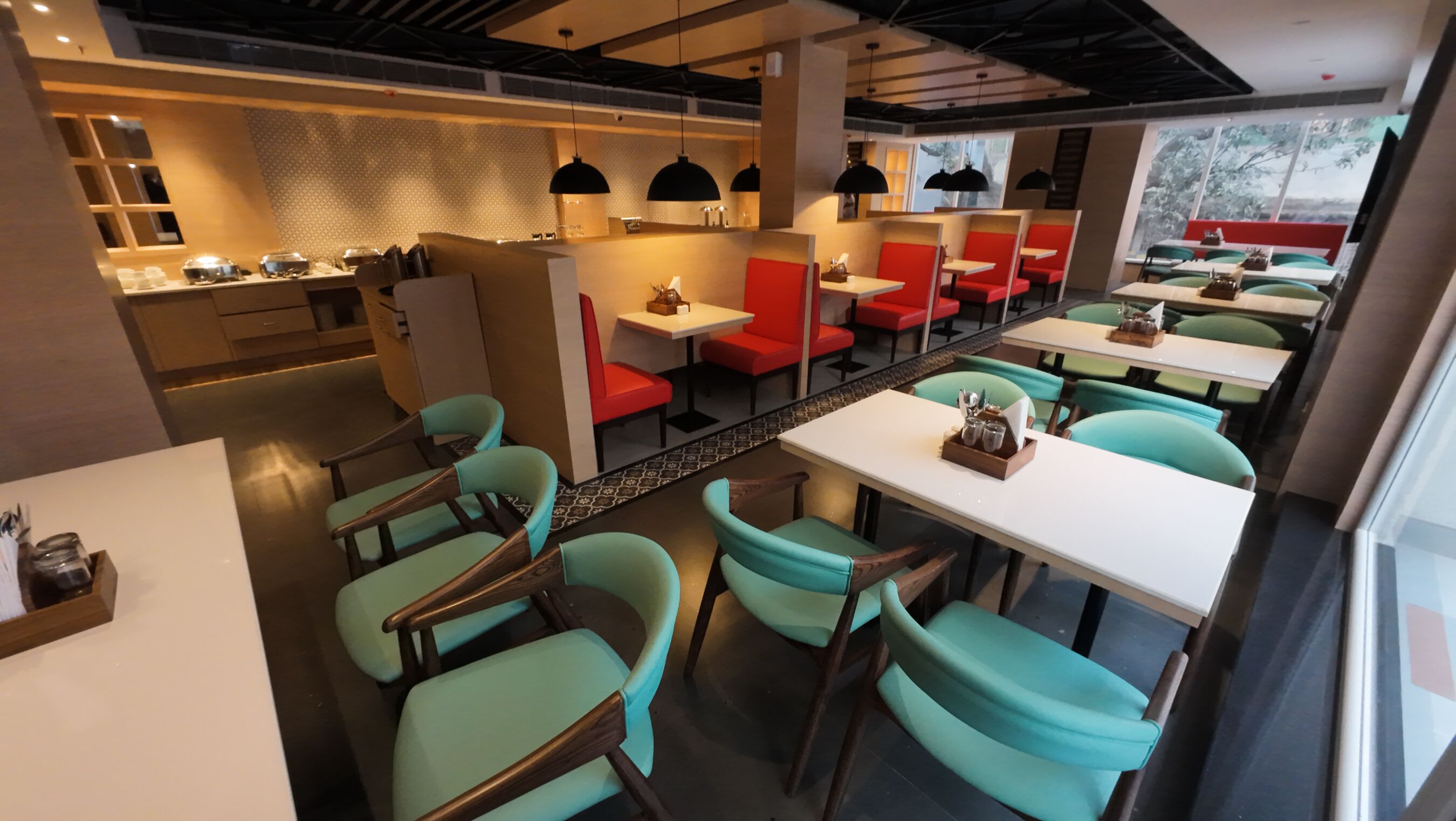 A modern restaurant with teal chairs and red booths, featuring a long communal table and pendant lighting.