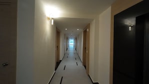 A long, narrow hallway with a light fixture on the left and a door on the right. - Hotel Sura Grand (Siliguri)