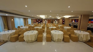A banquet hall with round tables, chairs, and a buffet area. - Hotel Sura Grand (Siliguri)