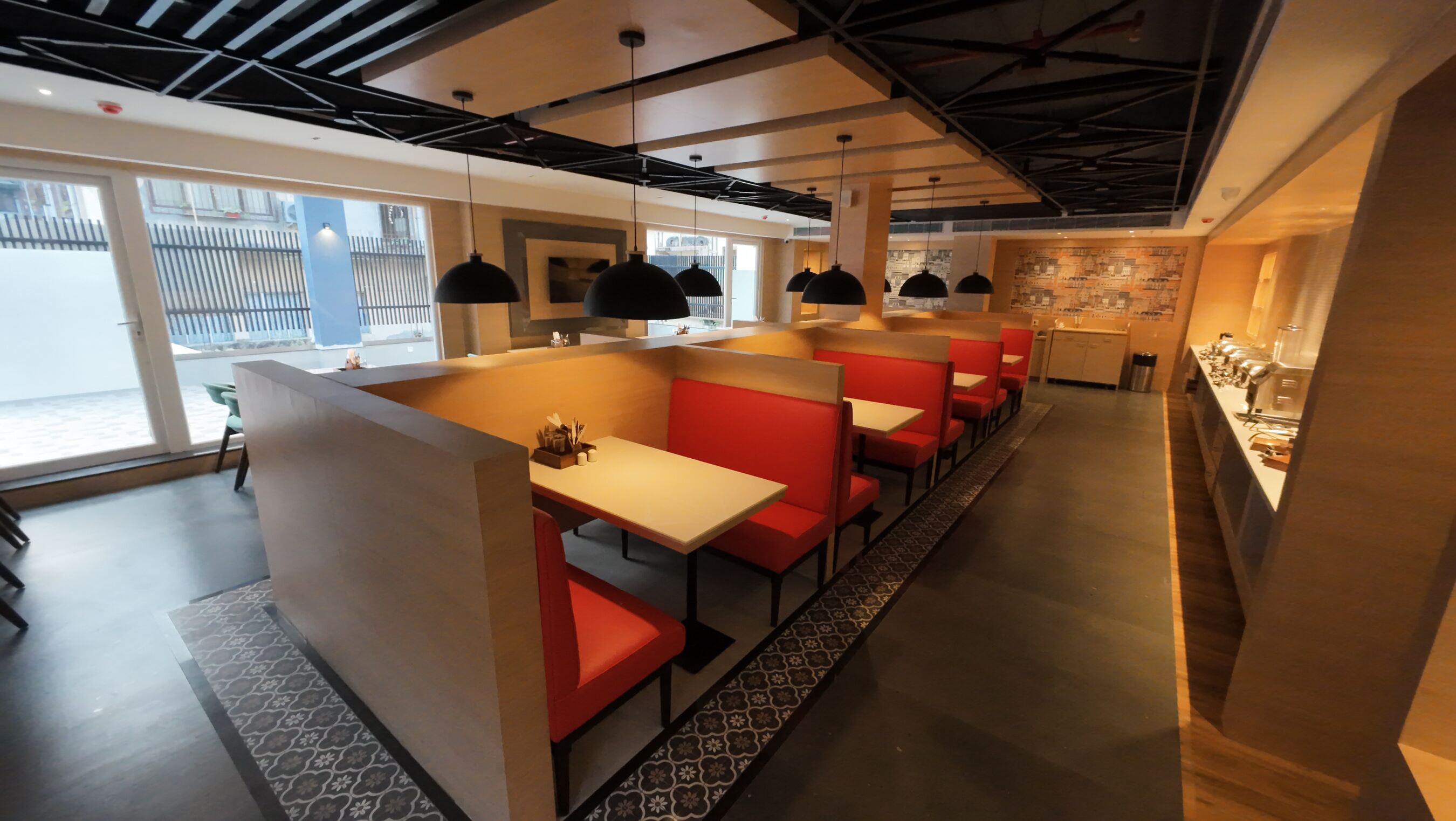 A modern restaurant with red booths and white tables, large windows, and a visible kitchen area.