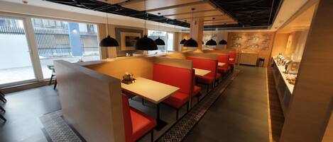 A modern restaurant with red booths and white tables, large windows, and a visible kitchen area.