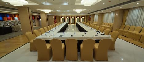Un salón de conferencias con una larga mesa, sillas color beige y una zona de buffet al fondo.