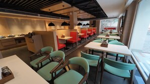A restaurant with teal chairs, red booths, and white tables. - Hotel Sura Grand (Siliguri)