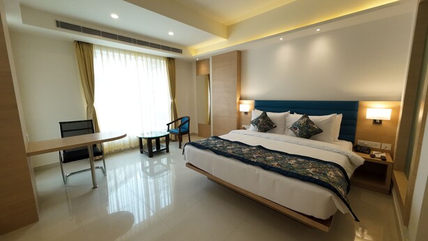 A modern hotel room with a large bed, bedside tables, a desk, and a chair. - Hotel Sura Grand (Siliguri)