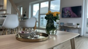 Una sala de estar moderna con una mesa de madera, un jarrón con rosas amarillas y una bandeja con vasos y un bol.