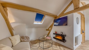 A cozy loft bedroom with a sloped ceiling, a skylight, a fireplace, a TV, and a comfortable sofa.