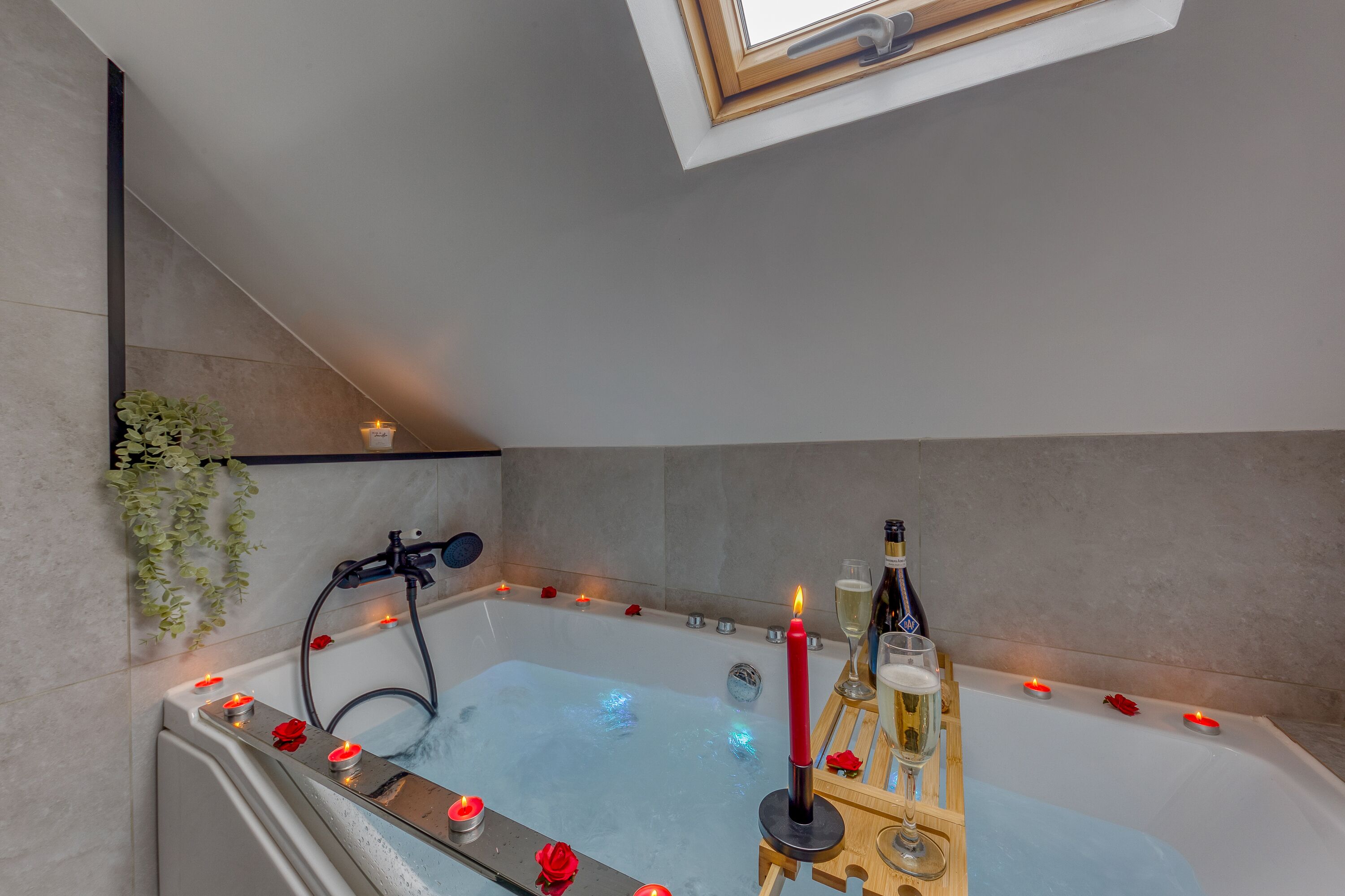 Une salle de bain moderne avec une baignoire sur pieds, des pétales de rose, des bougies et une bouteille de champagne.