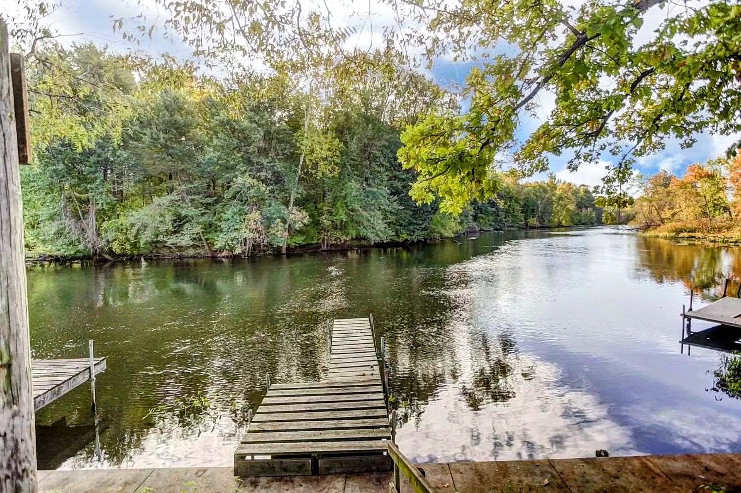 Une jetée en bois s’étendant dans un fleuve paisible, entourée d’une végétation luxuriante.