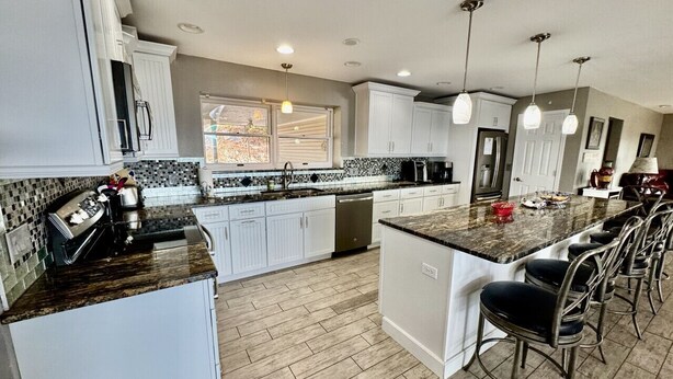 A modern kitchen with white cabinets, a marble countertop, and a central island with bar stools. - Hummingbird Hideaway (Branson)