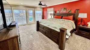 A bedroom with a large bed, a dresser, a nightstand, and a ceiling fan. There is a balcony with a view of the outside. - Hummingbird Hideaway (Branson)