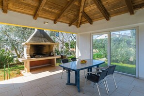 An outdoor patio with a barbecue grill, a table with chairs, and a view of greenery. - Premium Apartment Muha II (Kukci)