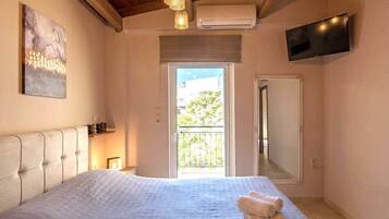 Ein Schlafzimmer mit einem großen Bett, einem an der Wand montierten Fernseher und einem Balkon mit Blick auf Grünflächen.