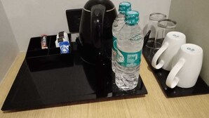 A hotel room's coffee station with a black tray, a black coffee maker, two water bottles, two white mugs, and a box of Nescafe coffee. - Komfort Stay (Guwahati)
