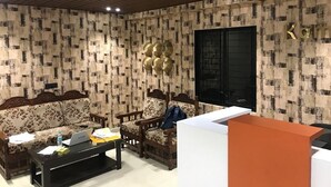 A living room with patterned wallpaper, a sofa, a coffee table with items, a chair, and a desk. - Komfort Stay (Guwahati)