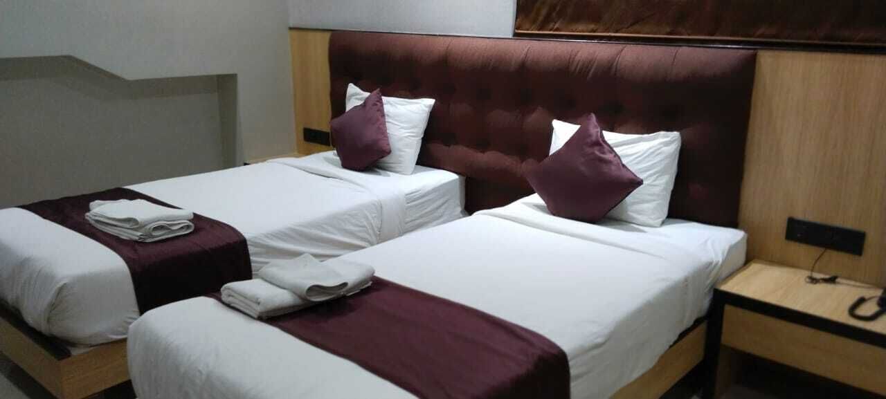 Ein Hotelzimmer mit zwei Einzelbetten, jeweils mit einer weißen Matratze und einem violetten Kopfteil. Auf jedem Bett liegen zwei weiße Kissen und am Fußende jedes Bettes ein gefaltetes weißes Handtuch.