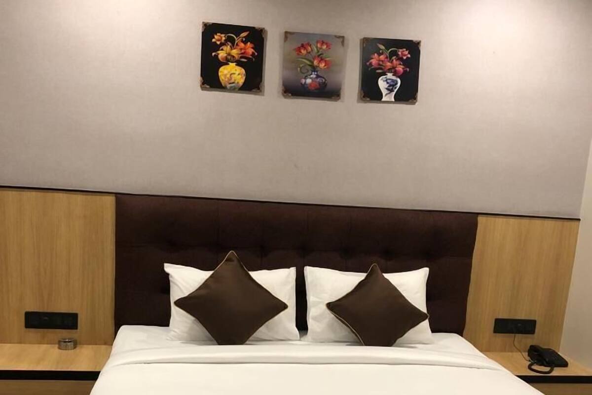 A neatly made bed with a brown headboard, white bedding, and two brown pillows. There are three paintings on the wall above the bed.