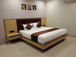 A modern hotel room with a large bed, wooden headboard, and two bedside tables. - Komfort Stay (Guwahati)