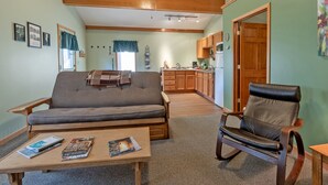A living room with a sofa, a coffee table with magazines, a leather chair, and a kitchen in the background. - Two-Level Forest Retreat | Near Bayfield (Bayfield)