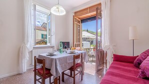 Un coin repas avec une table dressée pour deux personnes, un canapé rouge et une vue sur un village par des portes ouvertes.