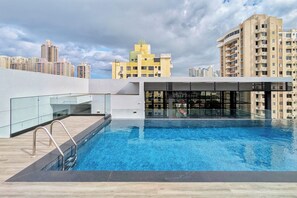 Une piscine sur le toit, dotée d’une balustrade en verre, et entourée d’immeubles de grande hauteur.