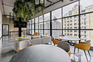 A modern office space with a large window, a sofa, a round table, and hanging plants. - w* | Warm 1BR in San Francisco w/ Balcony (Panamá)