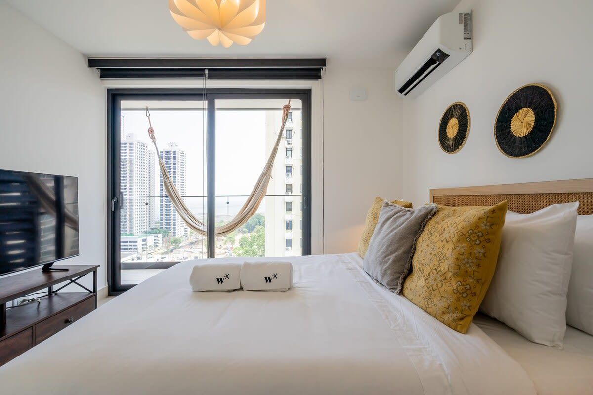 Habitación de hotel con cama, televisor, hamaca y vista a la ciudad.