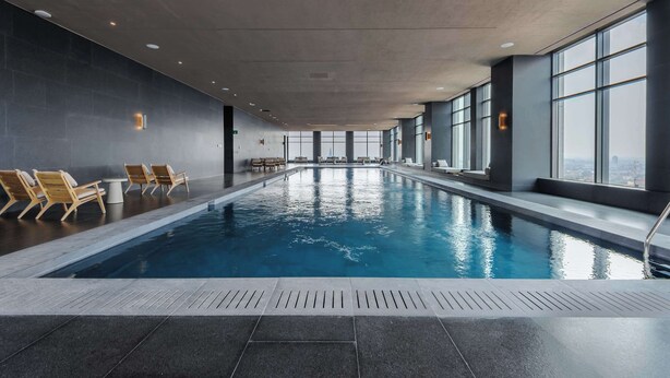 An indoor swimming pool with lounge chairs and tables, large windows, and a view of the city. - w* | Phenomenal 1BR with Amazing view in Cuauhtemoc (Ciudad de México)