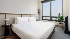 A modern hotel room with a large bed, a bedside table with a lamp, a potted plant, and a view of the city through a large window. - w* | Phenomenal 1BR with Amazing view in Cuauhtemoc (Ciudad de México)