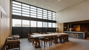 A spacious room with large windows, a long table with chairs, and a kitchen area with stools. - w* | Phenomenal 1BR with Amazing view in Cuauhtemoc (Ciudad de México)