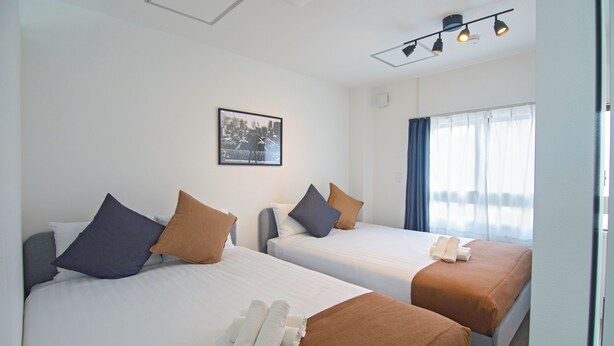 Two single beds with brown and blue pillows, white linens, and rolled towels. - Tabi Time Nishinagahori  (Osaka)