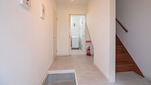 A narrow hallway with a wooden staircase on the right, a door at the end, and a fire extinguisher on the wall. - Tabi Time Nishinagahori  (Osaka)