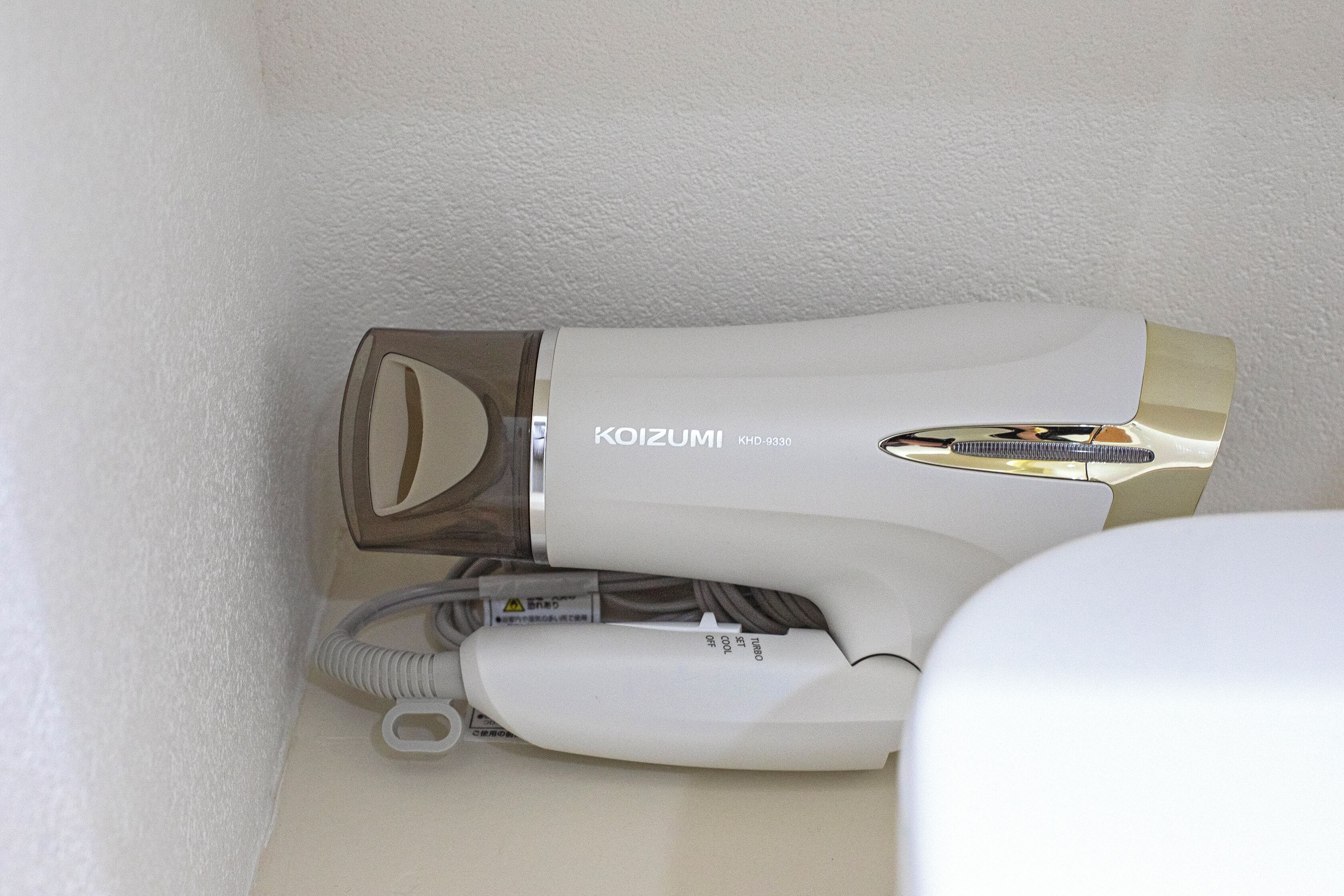 A hair dryer with the brand name 'KOIZUMI' and model number 'KHD-9330' in a bathroom setting.