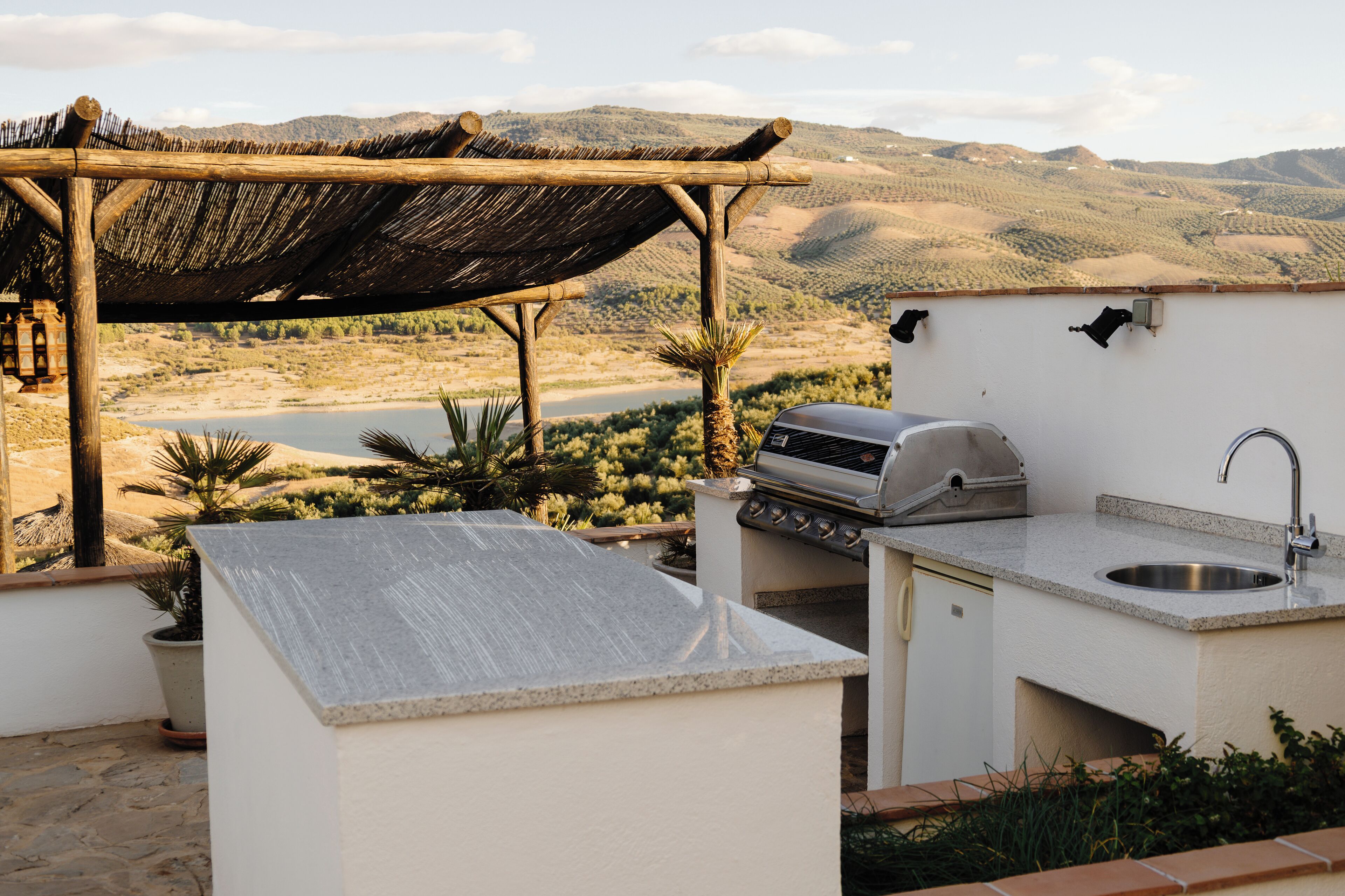 An outdoor kitchen area with a grill, sink, and a pergola providing shade.