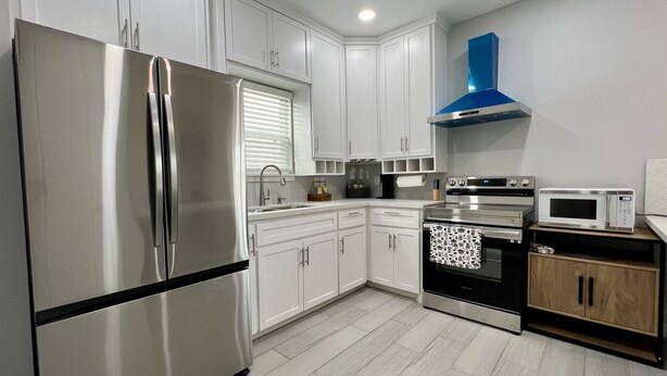Una cocina moderna con gabinetes blancos, electrodomésticos de acero inoxidable y una campana extractora azul.