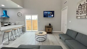 Una sala de estar moderna con un sofá gris, una mesa de centro redonda y una zona de cocina con horno y microondas integrados.