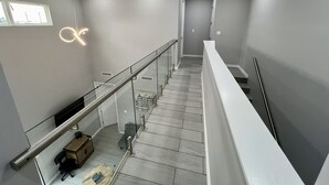 Un interior moderno con una escalera, barandillas de vidrio y una paleta de colores neutros y sobria.