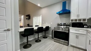 Une cuisine moderne avec des armoires blanches, une cuisinière en acier inoxydable, une hotte de couleur bleue et un coin bar agrémenté de tabourets noirs.