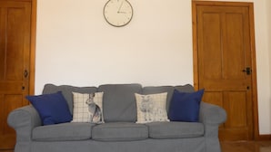 Un canapé gris agrémenté de coussins bleus et à motifs, une horloge murale et des portes en bois.