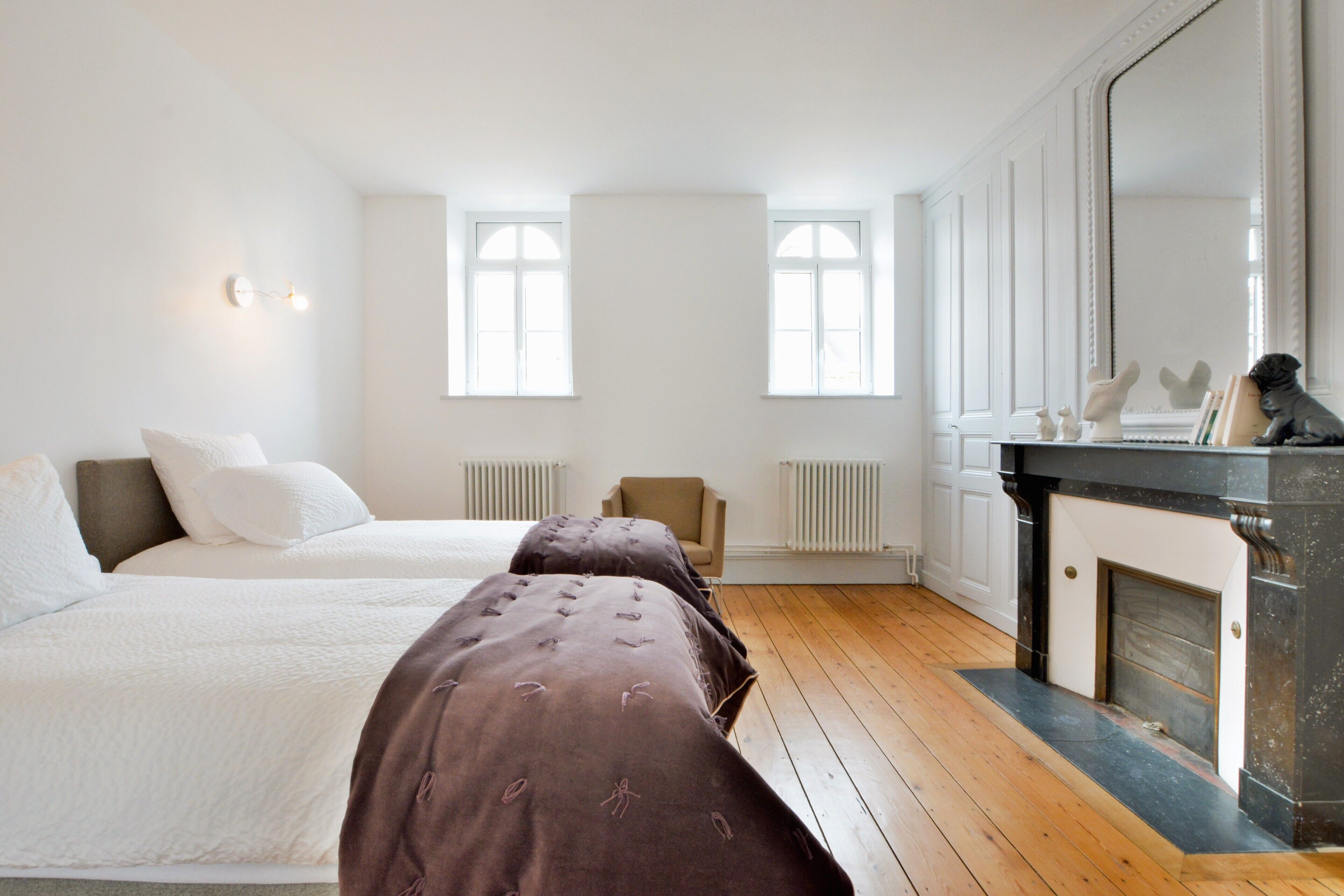 A bedroom with two beds, a fireplace, and a large mirror.