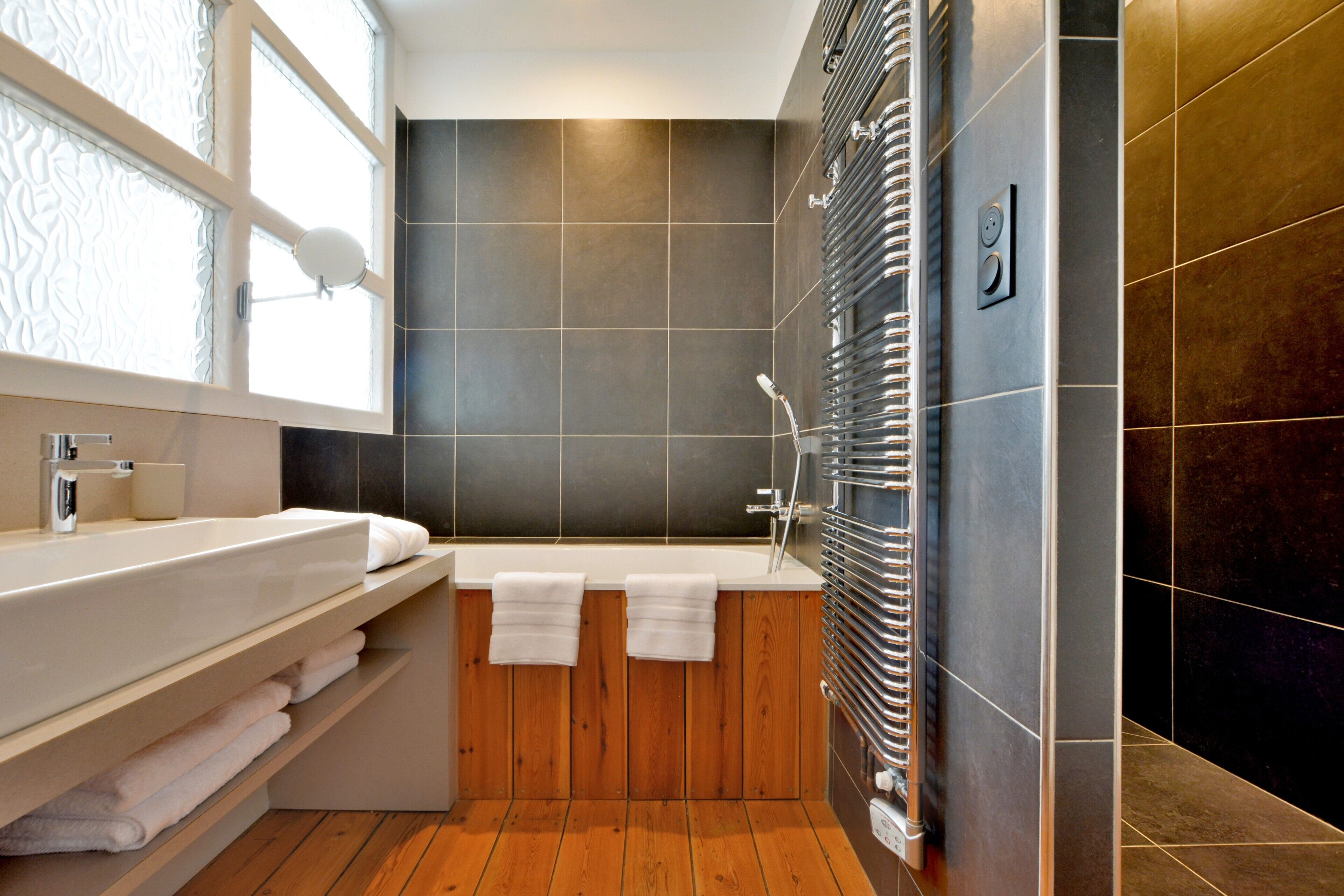 A modern bathroom with a wooden vanity, a large bathtub, and a wall-mounted towel rack.