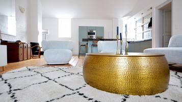 A modern living room with a round gold table, light blue armchairs, and a kitchen in the background.
